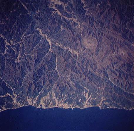 Image showing the oblique view of a section of the east-central coast of Korea and the backbone of the Taebaek-San Maek Mountains. Amidst the rugged hills you can see a shallow circular depression, nicknamed "The Punchbowl" during the Korean War.  Please have someone assist you with this. 