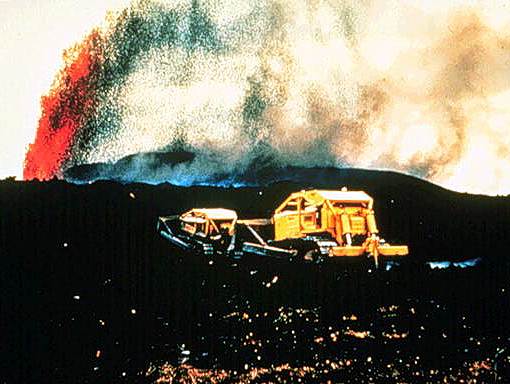 Image of a volcanic vehicle driving through volcanic ash with a volcano erupting in the background.
