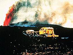 Image of a volcanic vehicle driving through volcanic ash with a volcano erupting in the background.  This image links to a more detailed image.