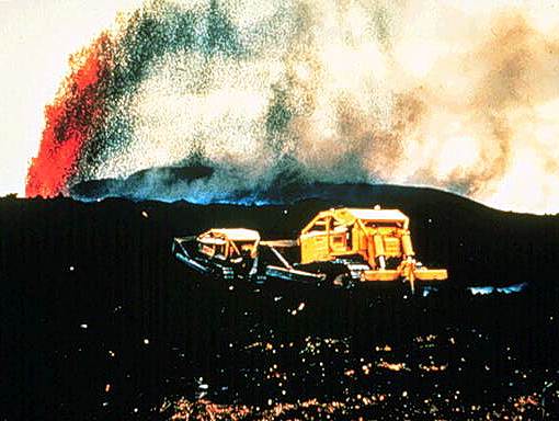 Image of a volcanic vehicle driving through volcanic ash with a volcano erupting in the background.