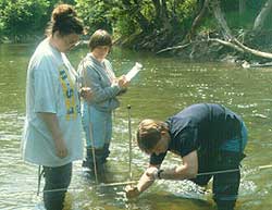 Image of some students measuring stream width with a meter tape, depth with a meter stick, and flow with a flow meter along Wheeling Creek.